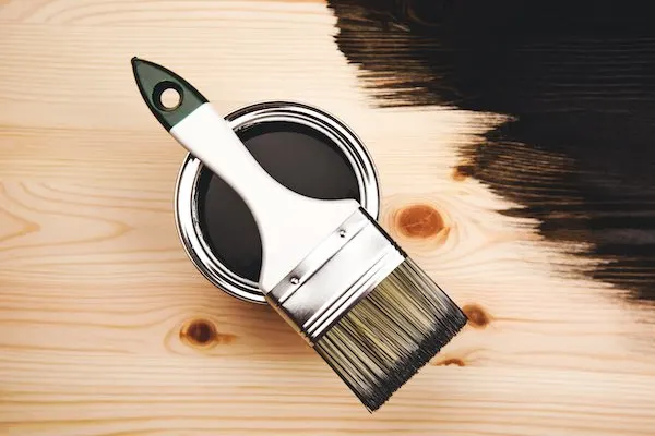 Black paint in a paint can lay on top of a piece of wood.
