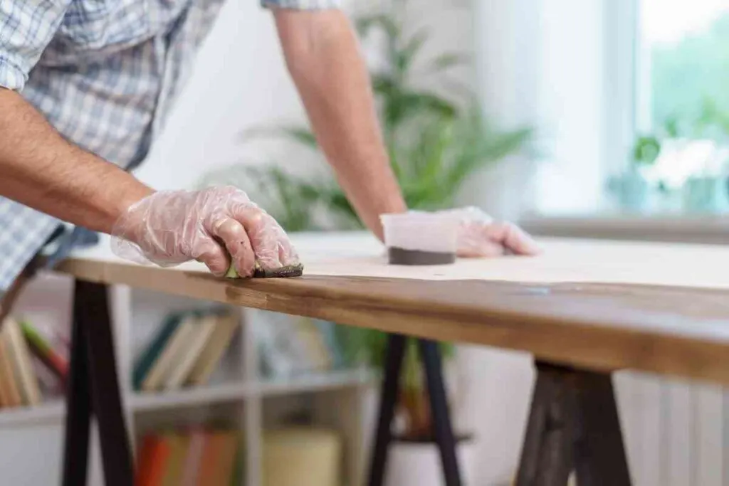 A man's hand using a rag to apply stain to a table