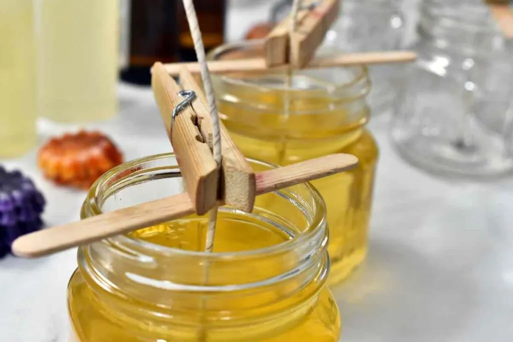 Using a clothespin and popsicle stick to secure a wick in a candle