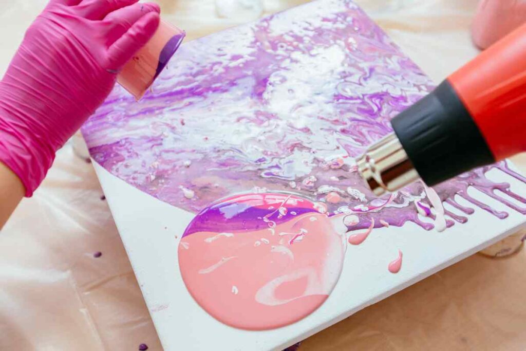 Using a hairdryer to manipulate purple and pink paints that have been poured on a canvas