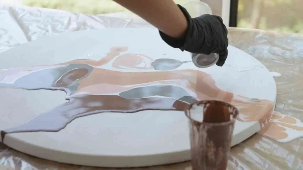Paint pouring on a round canvas with paint colors in greys and beiges