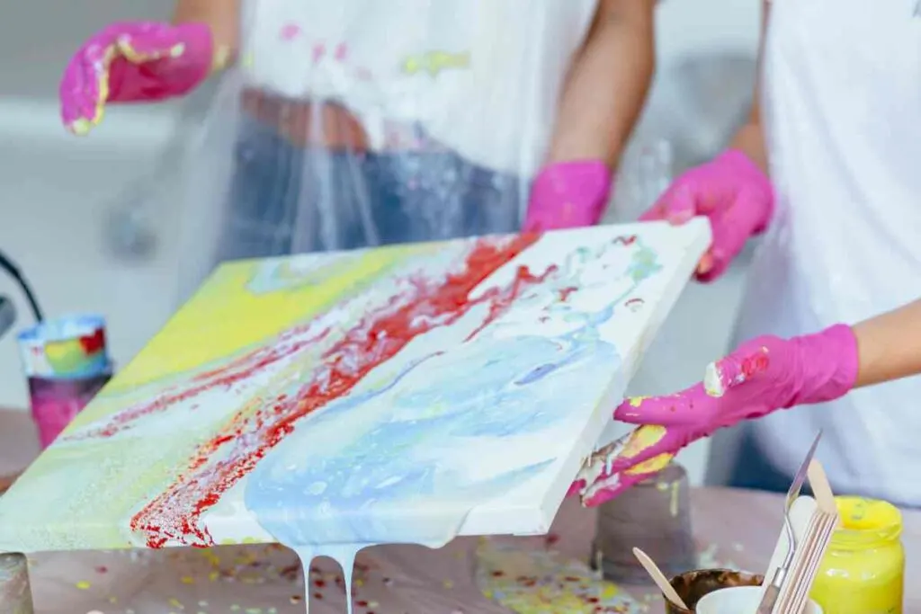 Hands holding a colorful canvas with paint pouring supplies on the table