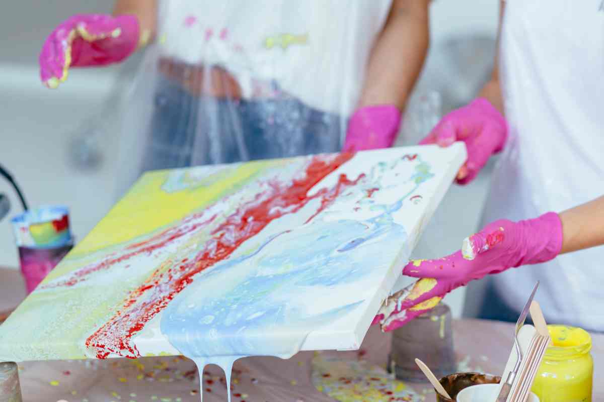 Hands holding a colorful canvas with paint pouring supplies on the table