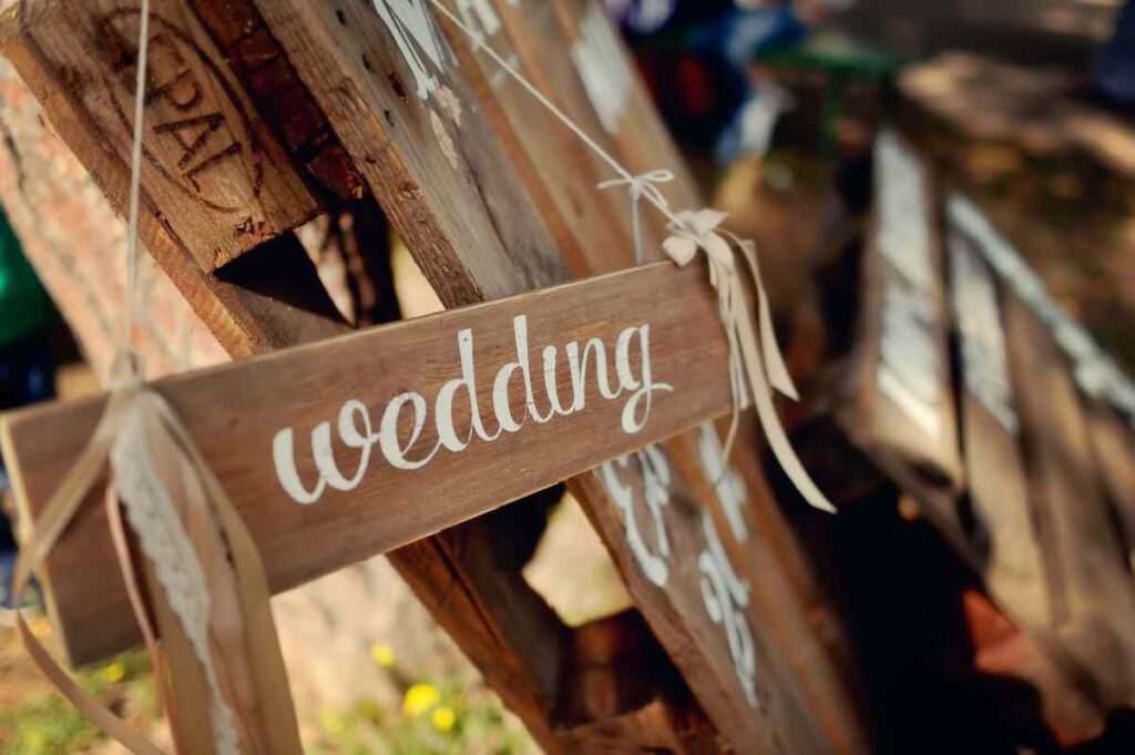 Wooden sign painted with the word wedding in white hanging on a pallet
