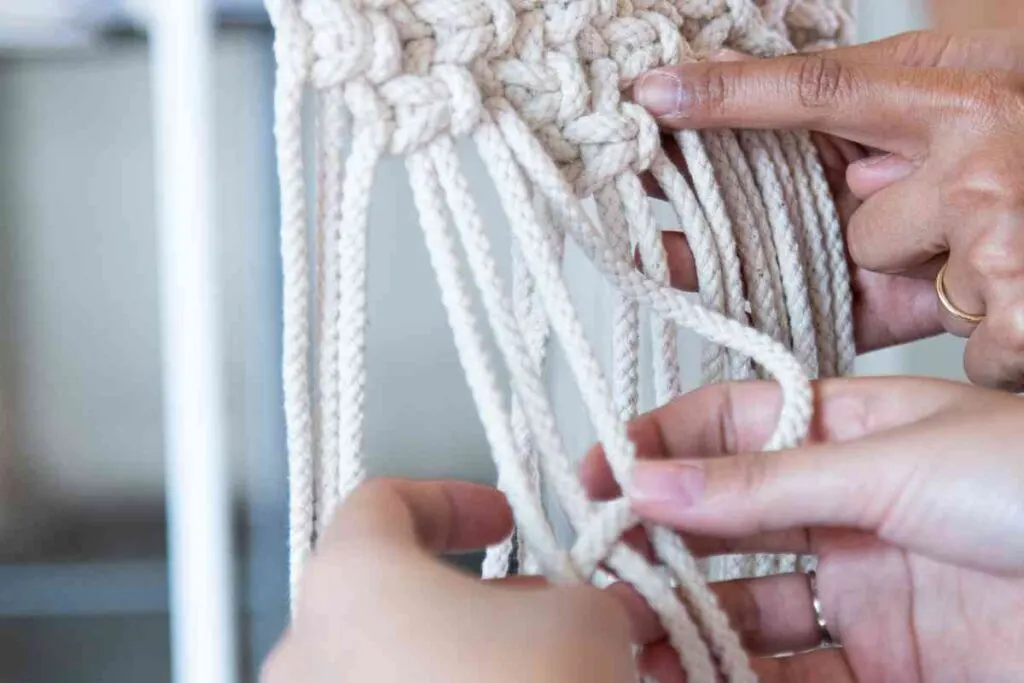 Hands of one woman teaching another how to do macrame