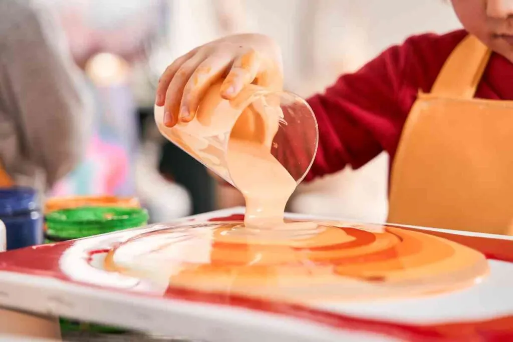 A person pouring acrylic paints on a canvas