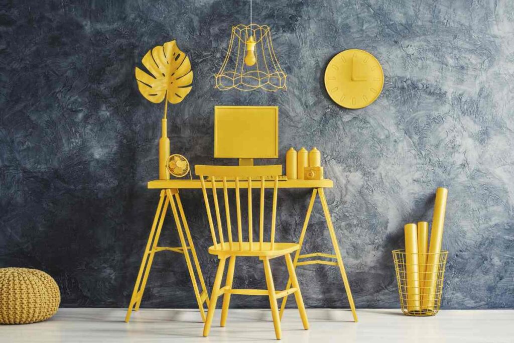 Room with a grey wall and the desk, computer, wall hangings, and decorations all spray painted yellow