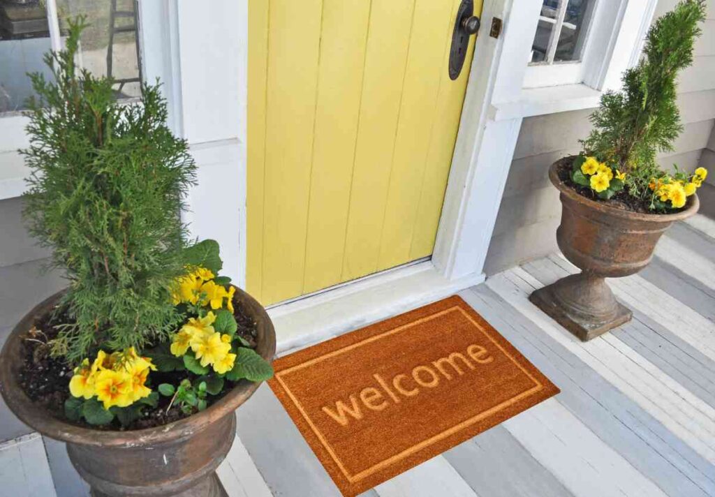 Front porch floor painted in grey and white stripes with a yellow door and urns with yellow flowers