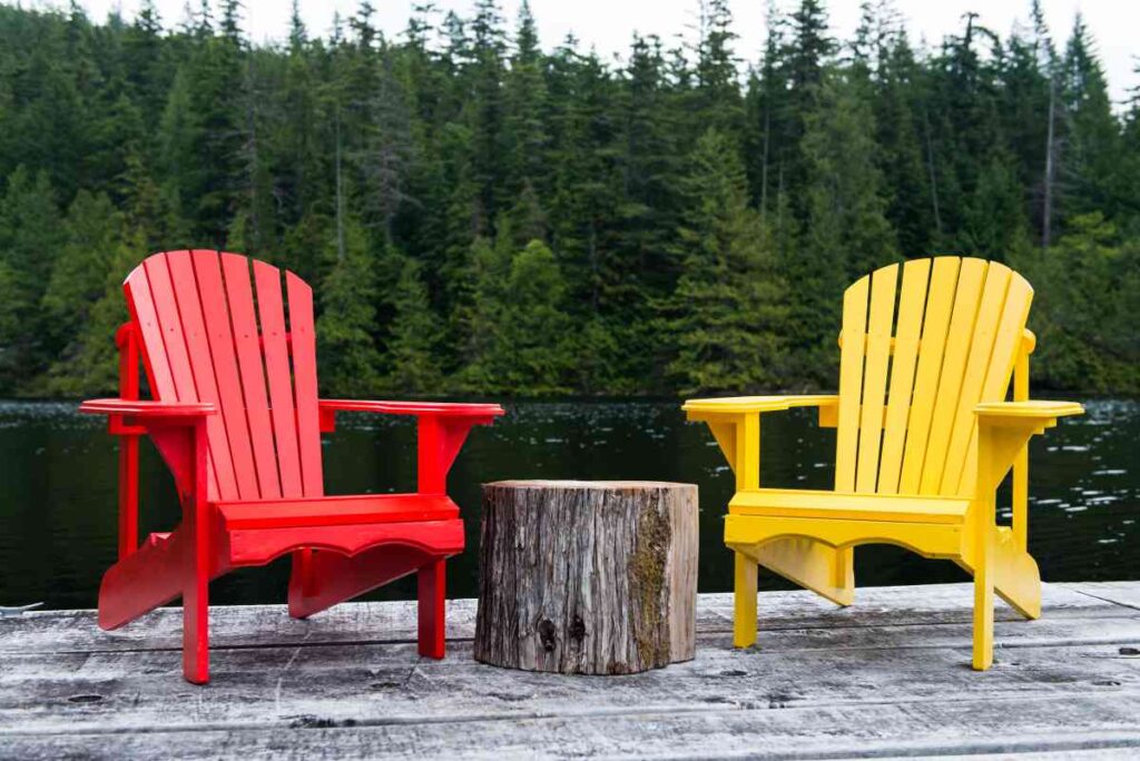 red and yellow adirondack chairs next to a wood log side table with trees in the background