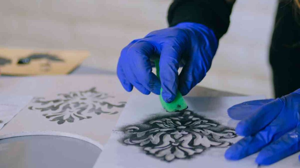 Using a sponge and black paint to add a stenciled design to a piece of furniture
