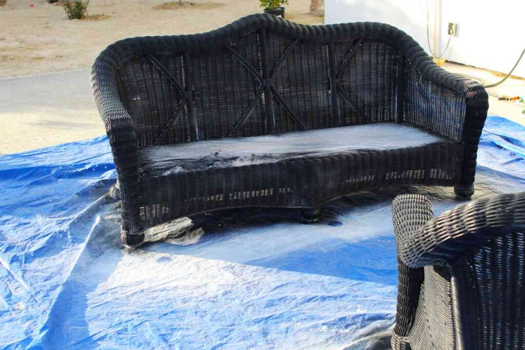 An outdoor sofa in the process of painting wicker furniture black