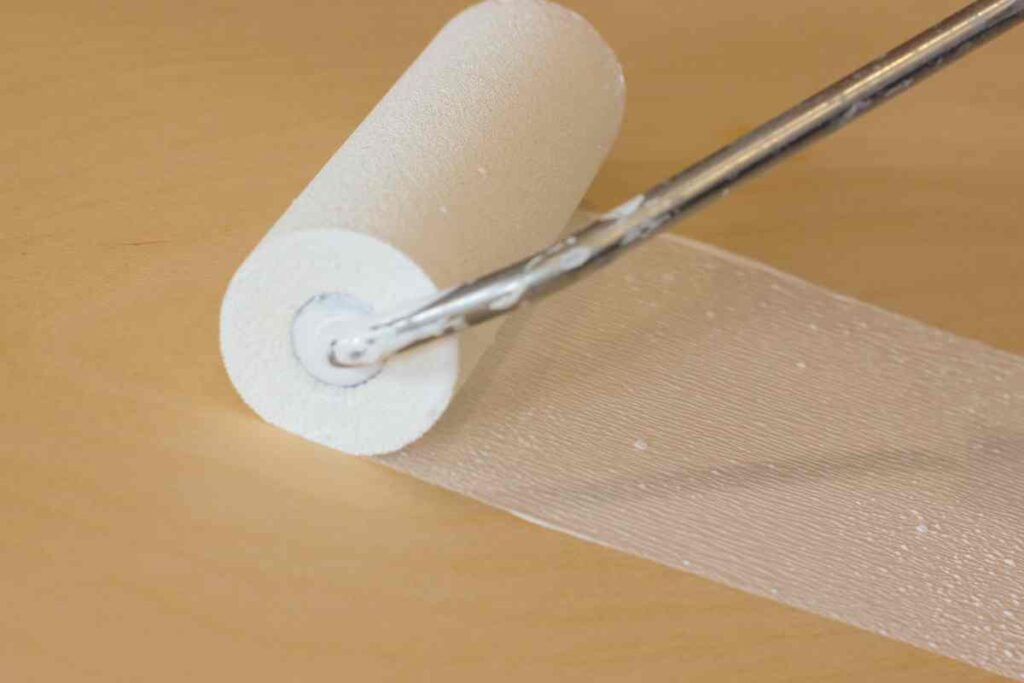 Close up of foam roller with white paint being used on a piece of gold furniture