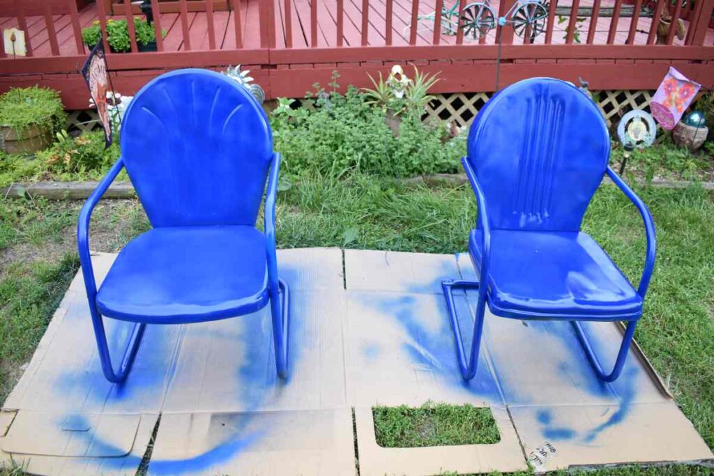 Two chair spray painted blue and drying on a piece of cardboard