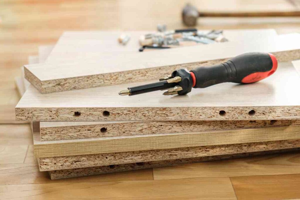 A stack of disassembled particle board furniture and a screwdriver