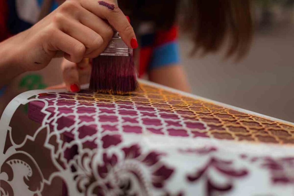Using a stencil to apply a gold pattern to a purple dresser