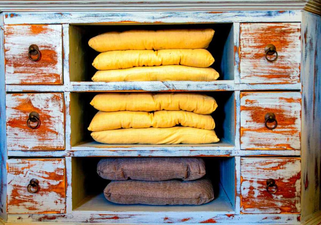 Wooden antique shelf with drawers painted blue and orange with yellow cushions in cubbies