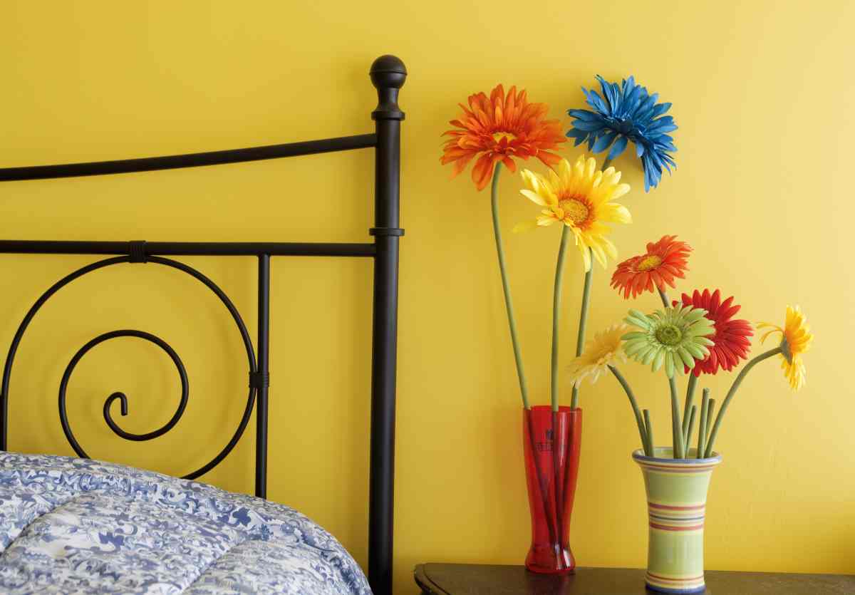Yellow wall, black bedframe, and vases with yellow and blue flowers are great yellow bedroom decorating ideas
