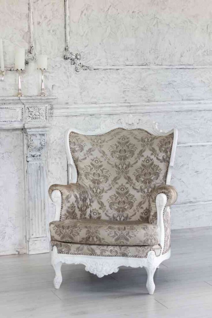 White accented wingback chair with grey damask material against a white block wall