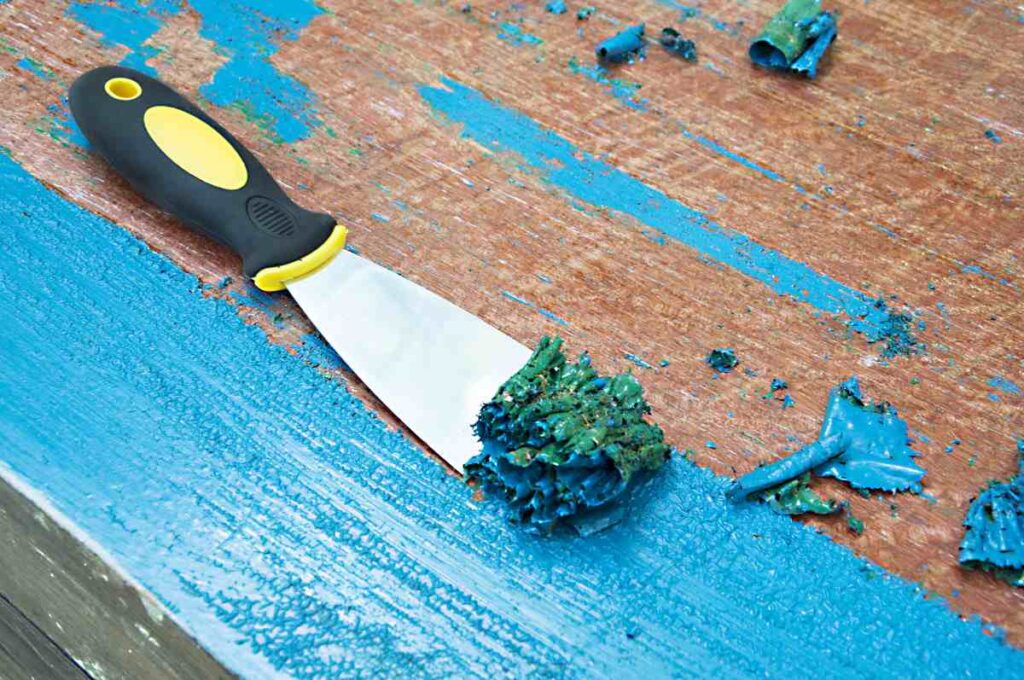 Stripping blue paint off a table before using one of the ideas for refinishing furniture