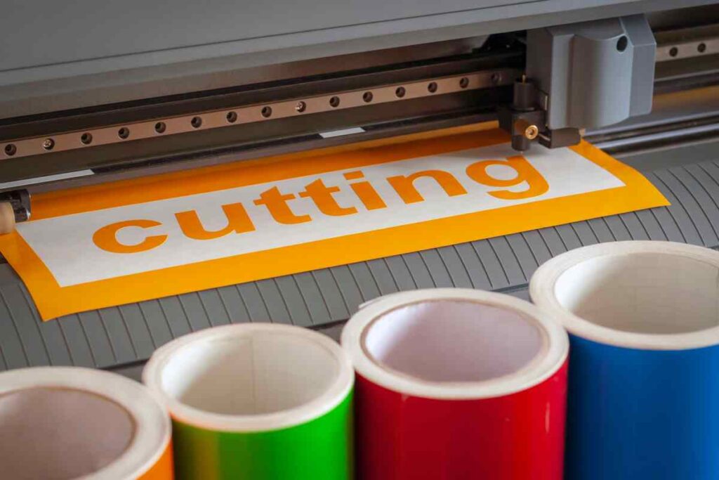Words being cut on a best vinyl cutting machine with rolls of colorful vinyl in the foreground