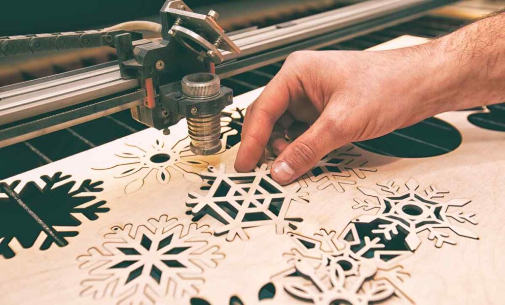 Man using the best wood cutting machine to cut a sheet of snowflakes
