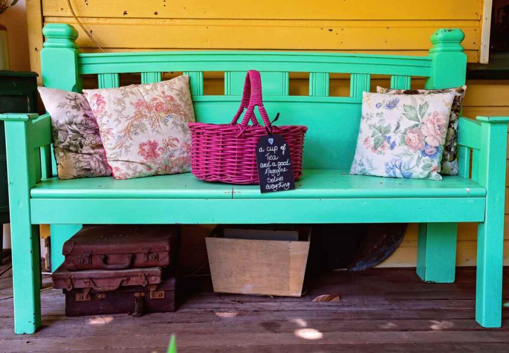 Antique bench painted green with colorful throw pillows and a purple basket