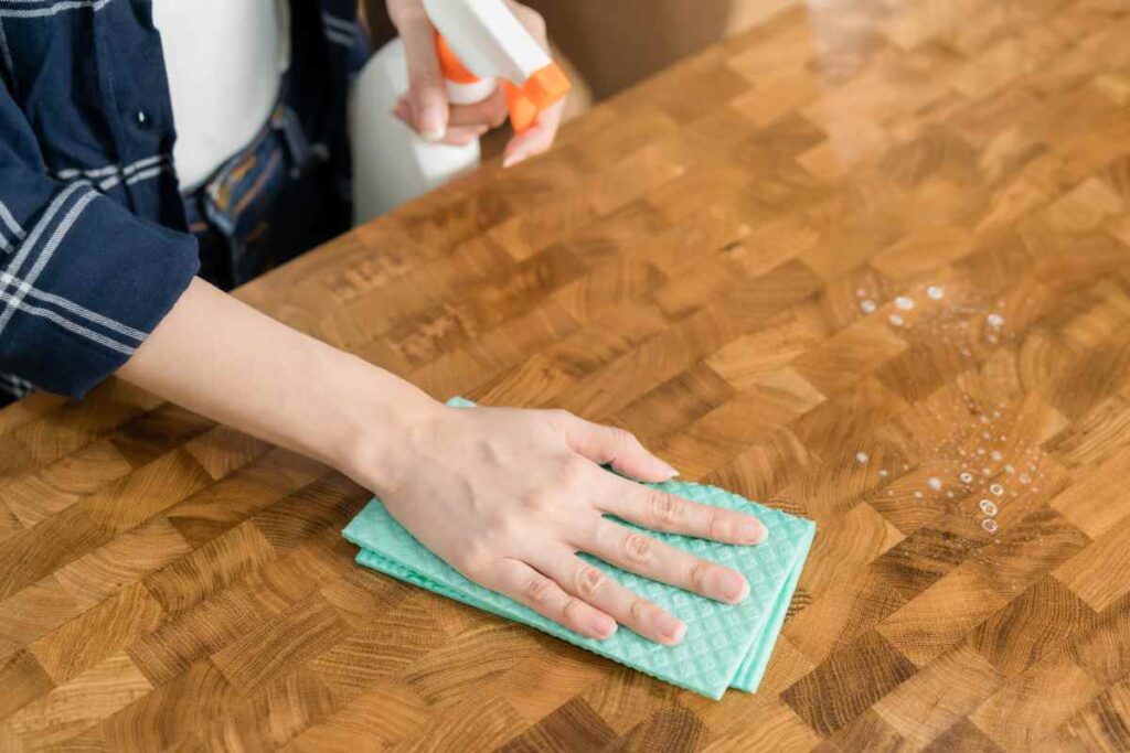 Using a microfiber cloth and spray cleaner on a piece of wood furniture