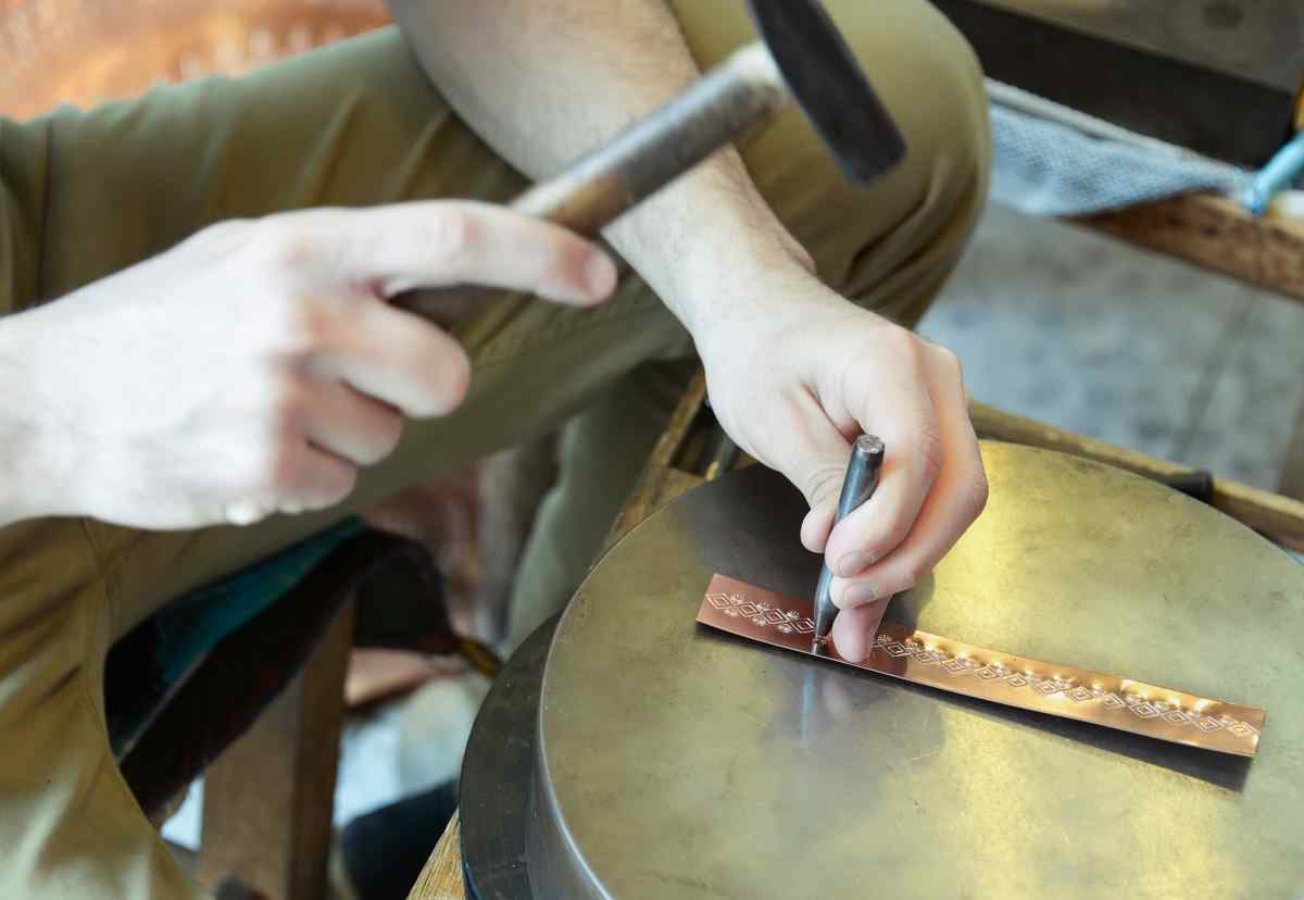 A person demonstrating stamping metal jewelry by stamping designs on a copper bracelet