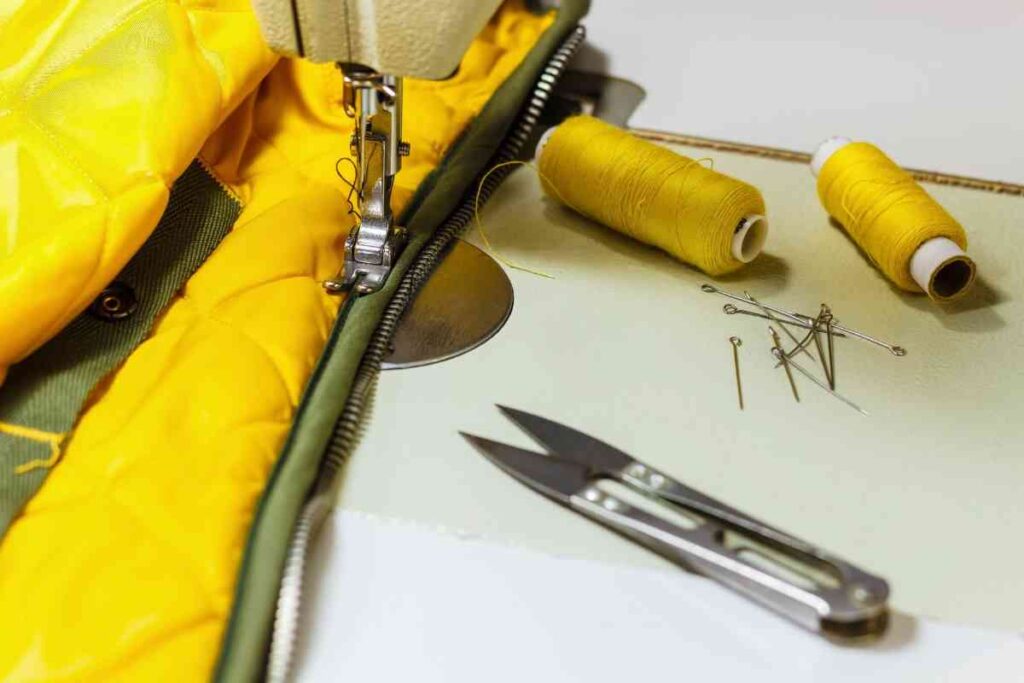 A yellow and green jacket on a sewing machine with yellow thread and scissors nearby