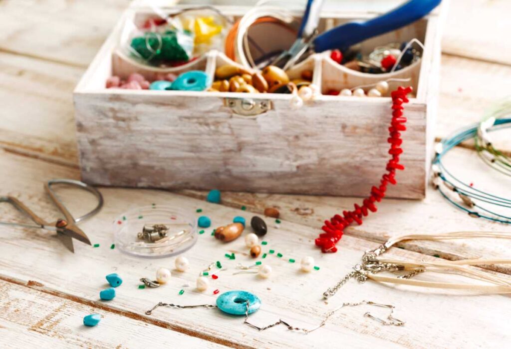 A wooden box with beads, scissors, and other tools needed for jewelry making