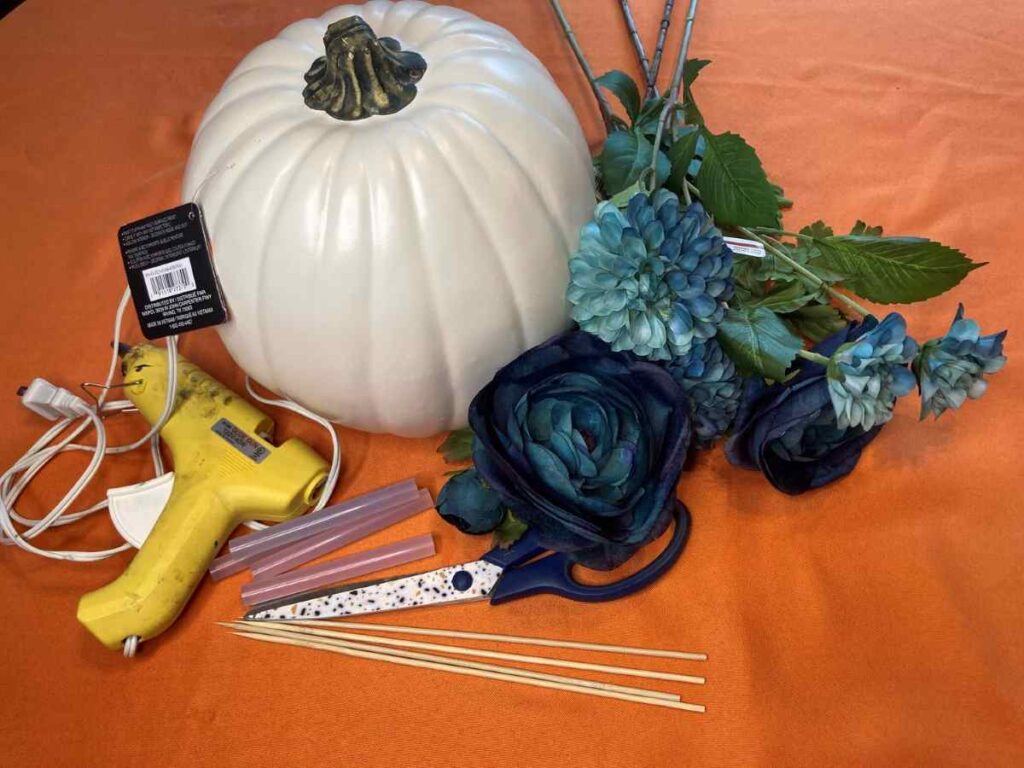 Picture of supplies needed for a fall centerpiece including a pumpkin, flowers, and a hot glue gun