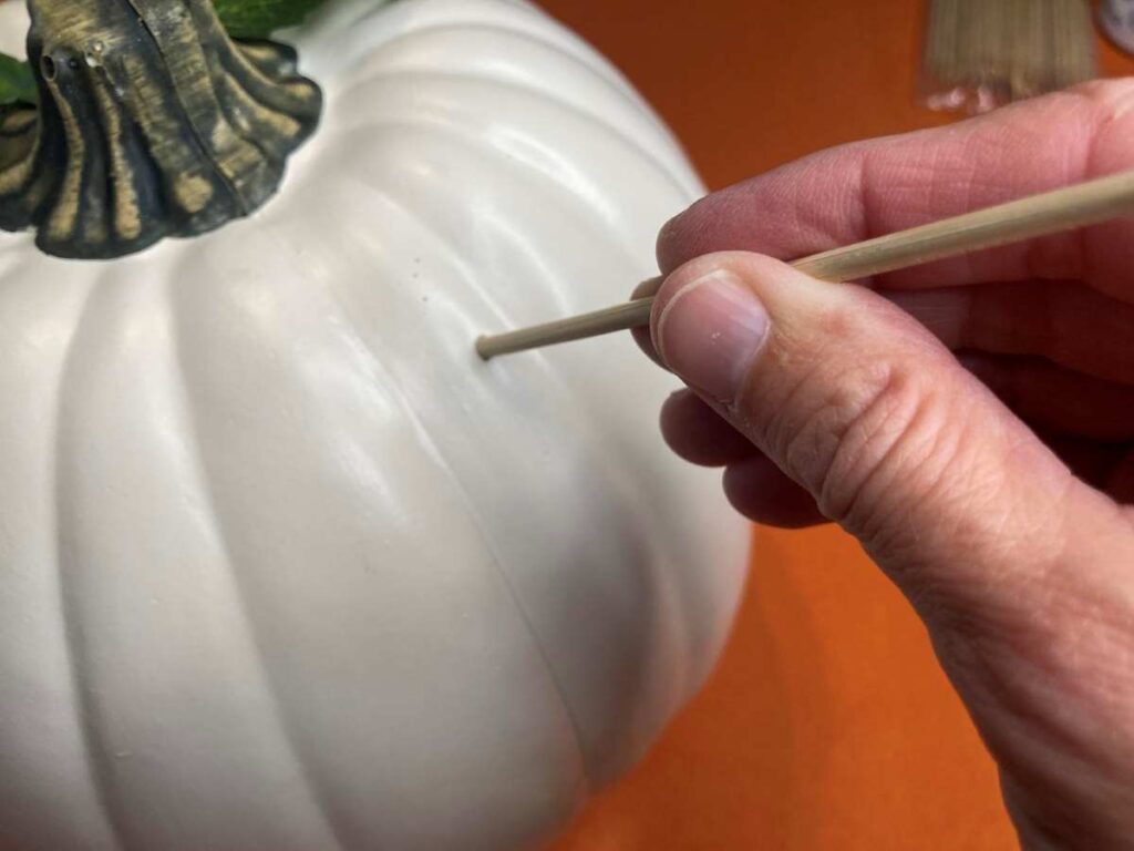 Using a skewer to poke a hole in a faux pumpkin for leaves and flowers