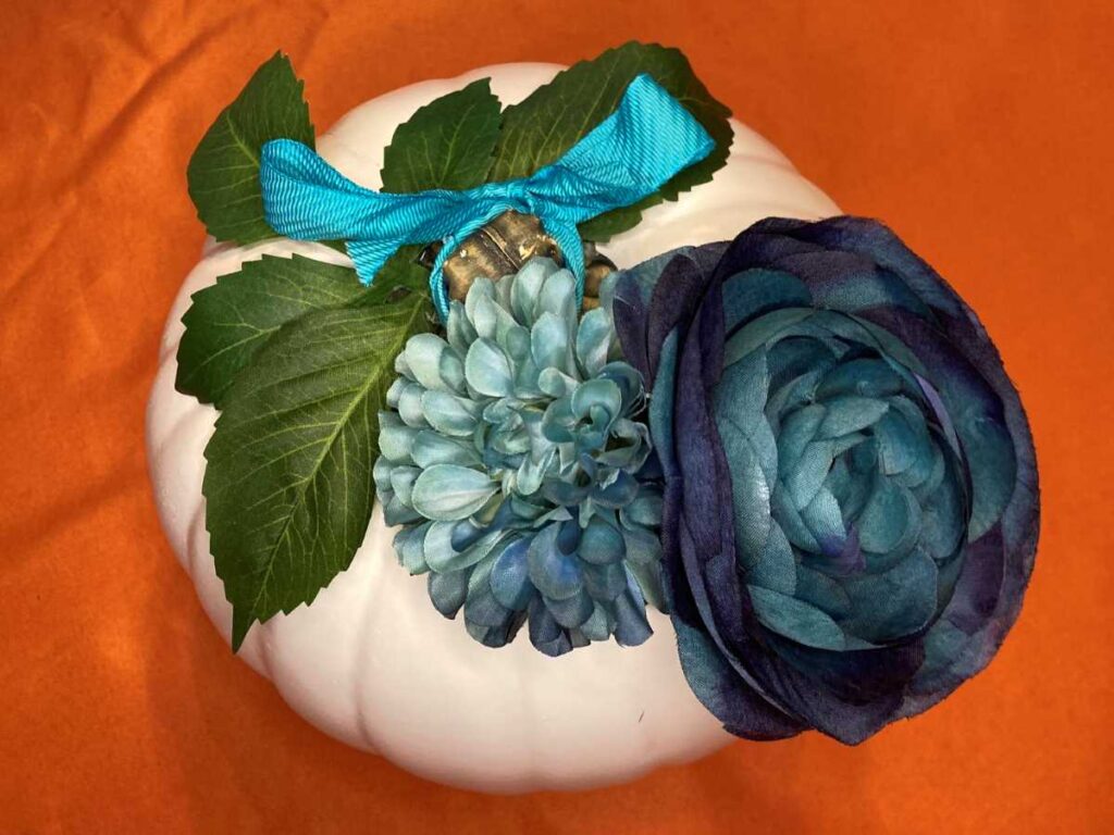 white pumpkin with blue flowers and ribbon and greenery
