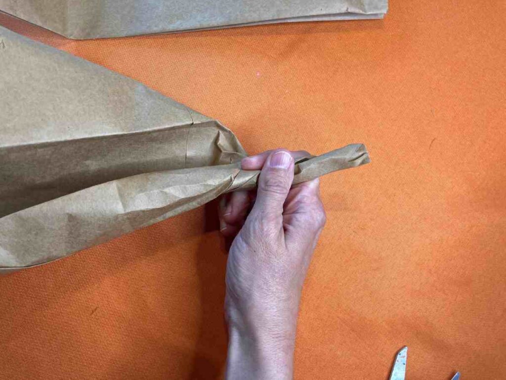 Twisting a brown paper bag to make the stem of a pumpkin