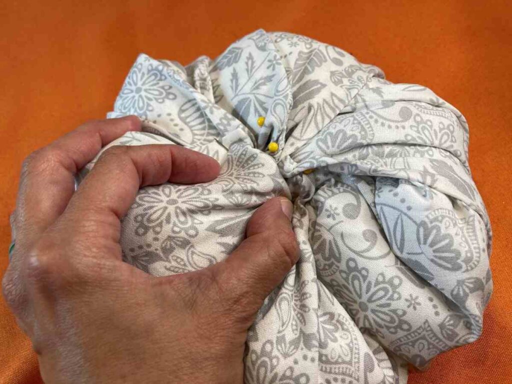 Using pins to hold fabric in place over batting to make a pumpkin