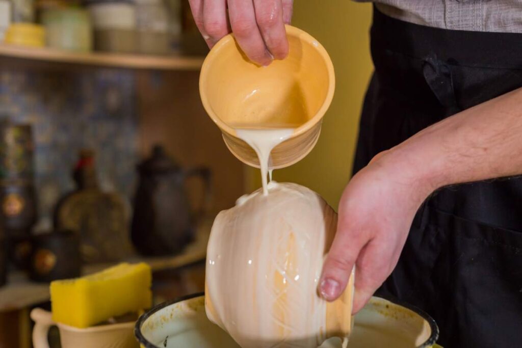 A person pouring glaze onto pottery