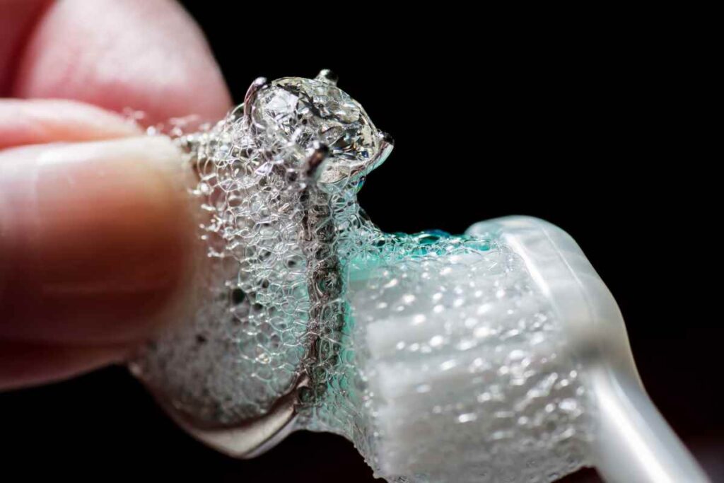 Using a soft toothbrush and soapy water to clean a metal and diamond ring