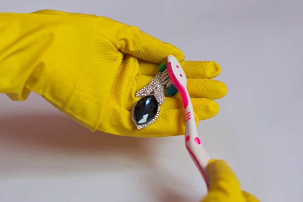 A person wearing gloves and using a soft toothbrush to clean metal jewelry