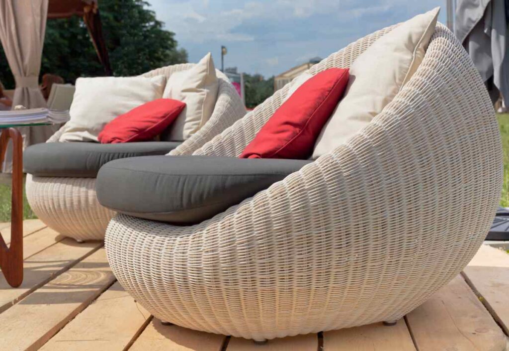 Two off-white oversized wicker chairs with red, grey, and white pillows