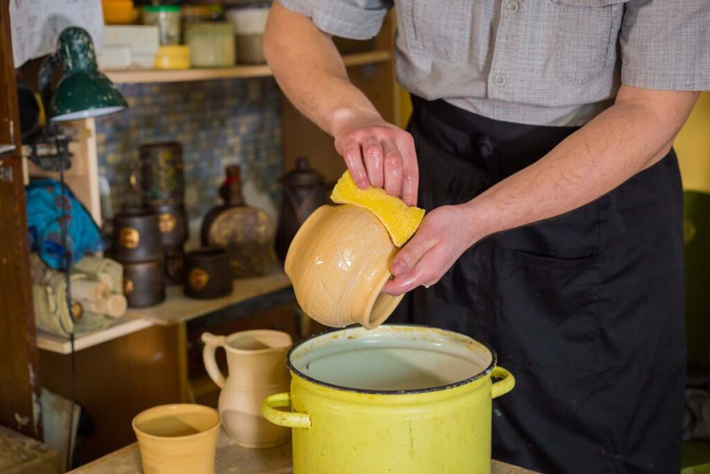 A person using a sponge to apply glaze to pottery