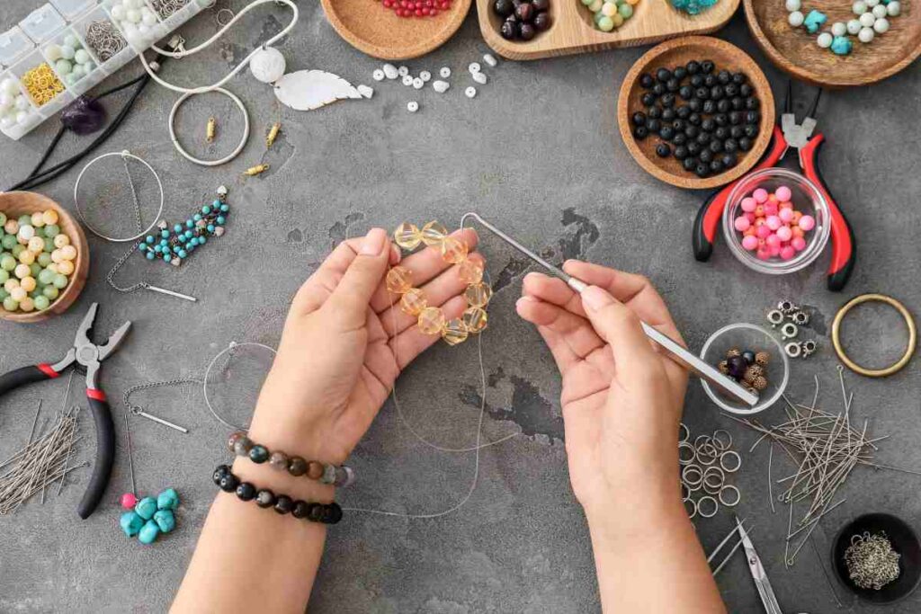 A woman making a beaded bracelet with lots of jewelry making ideas displayed on her work table
