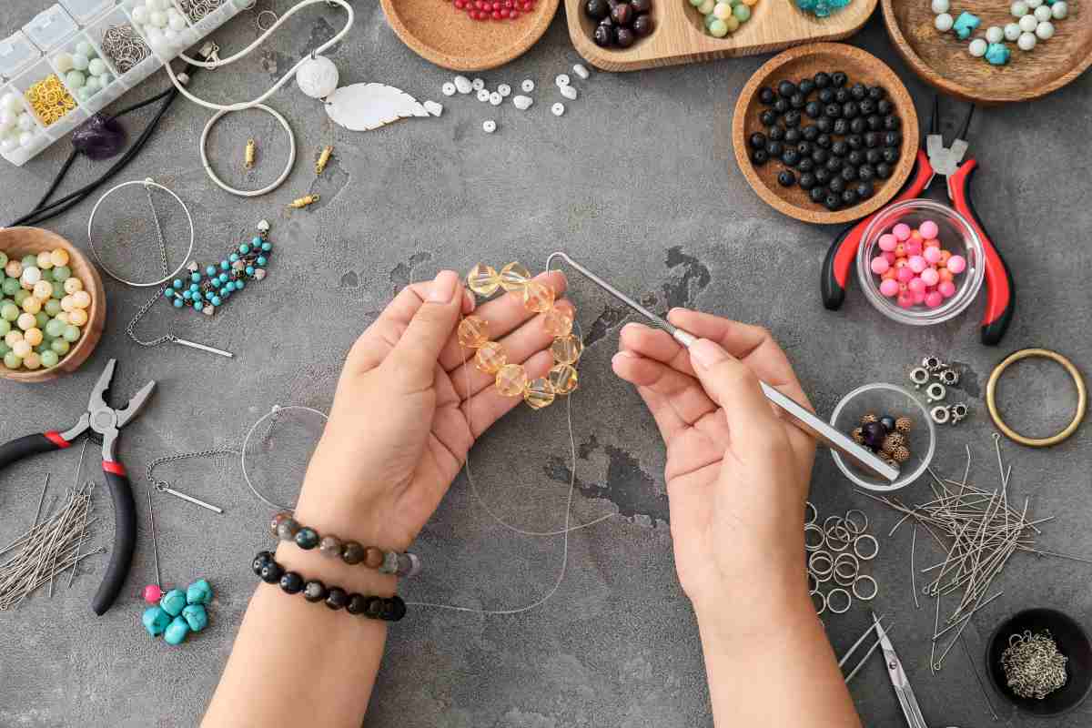 A woman making a beaded bracelet with lots of jewelry making ideas displayed on her work table