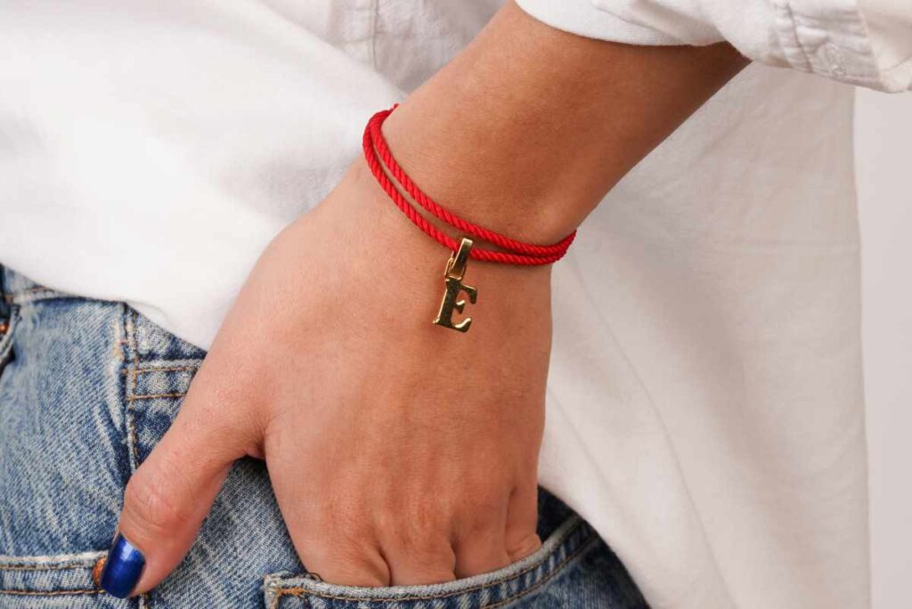 Woman wearing a red string bracelet with an initial E as a charm