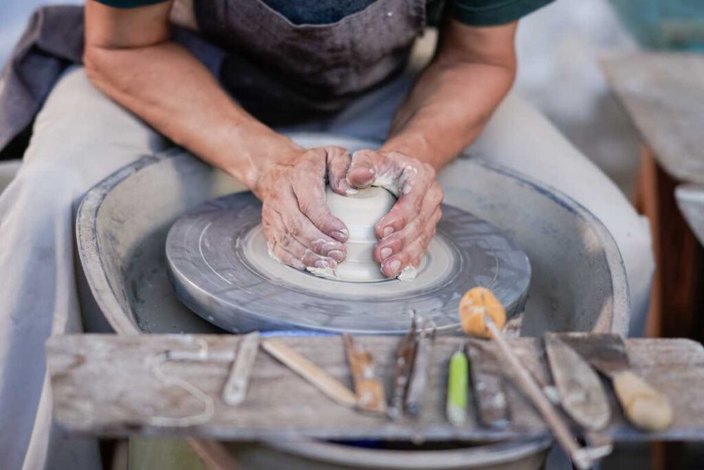 Artisan using a pottery wheel with his tools lined up in the foreground