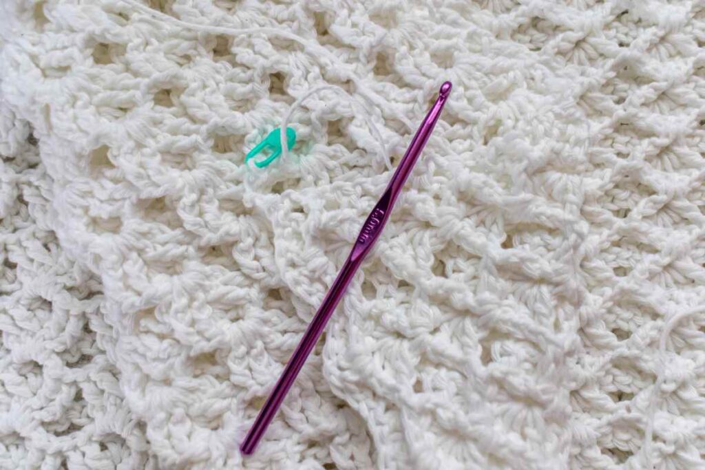 Crocheted blanket with stitch marker and crochet hook