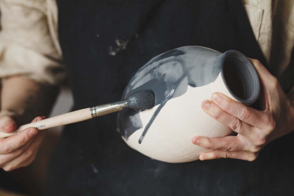 A person brushing glaze onto pottery