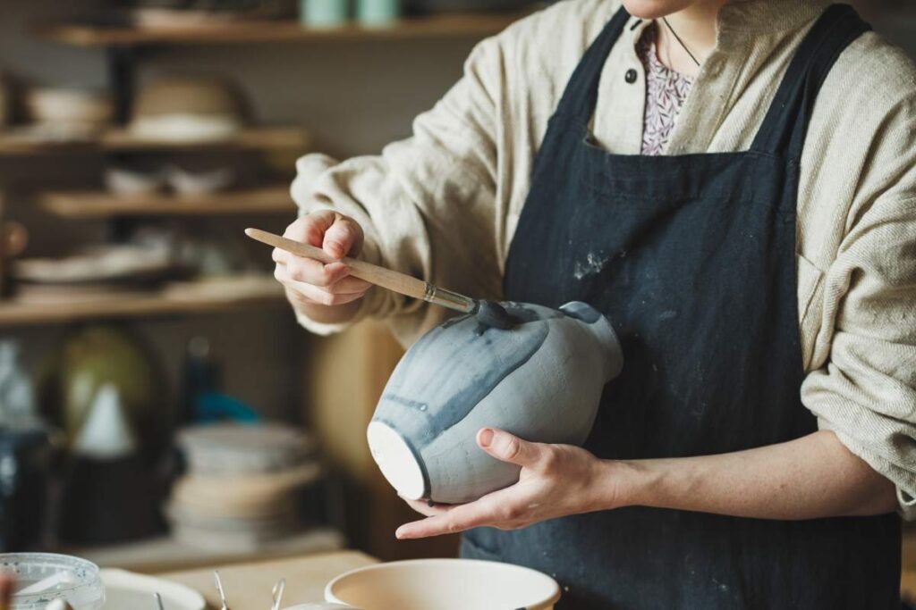 Artist brushing pottery glaze onto a vase.  Pottery glaze types