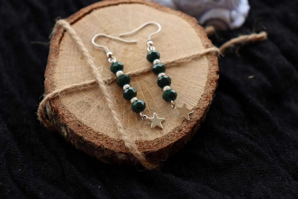 A pair of green and white beaded earrings displayed on a wood slice