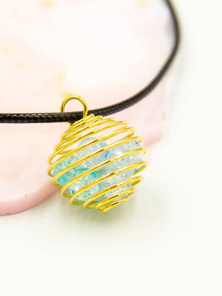 Gold cage pendant with blue crystal inside and black leather cord