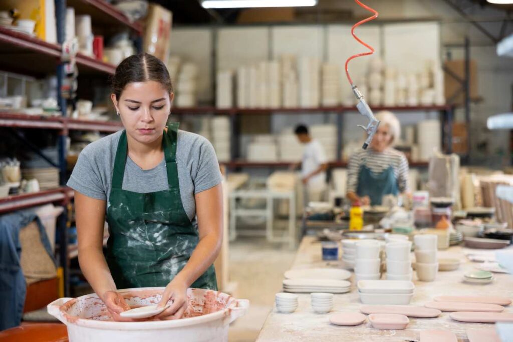 A woman dipping pottery into a bucket of glaze